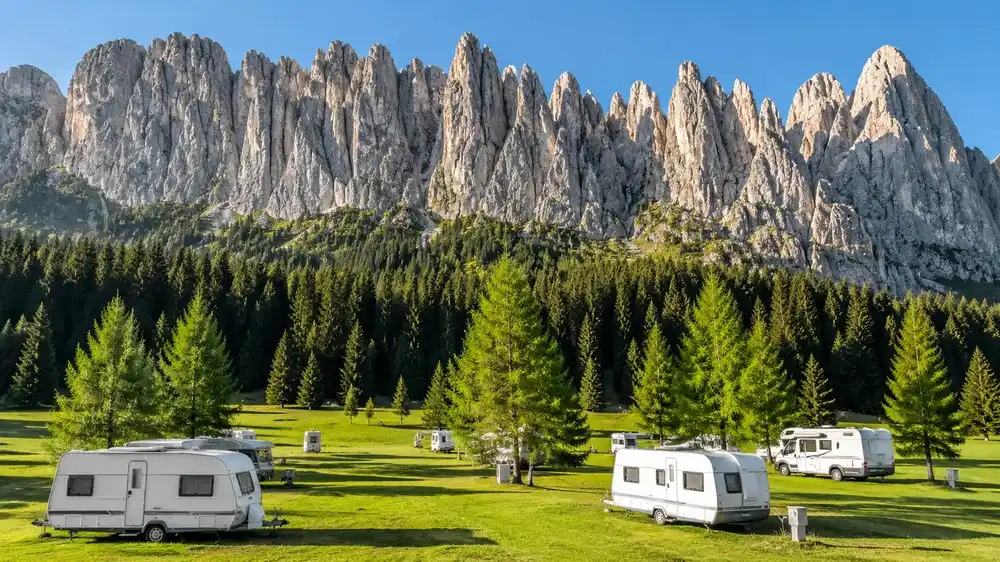Karavany na zelené horské louce pod skalními věžemi Dolomit